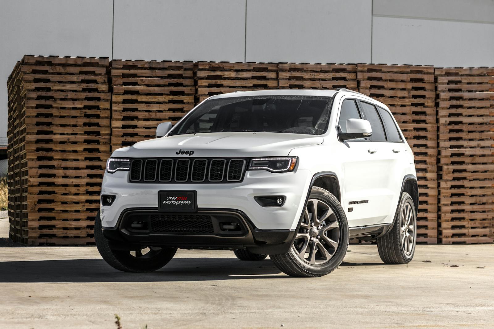 Auto, A sleek white Jeep Grand Cherokee parked in front of stacked wooden pallets, showcasing its luxury features.